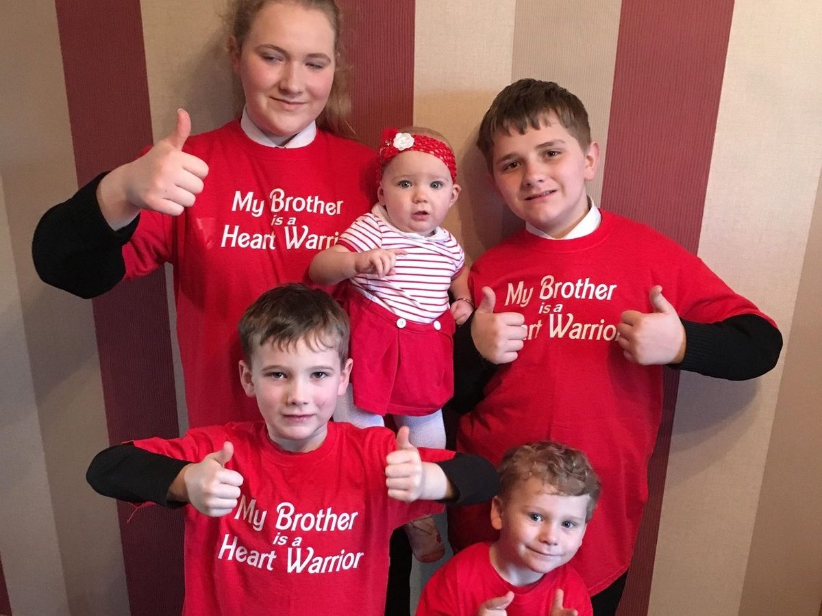 a family wearing red t-shirts saying 'My brother is a heart warrior'